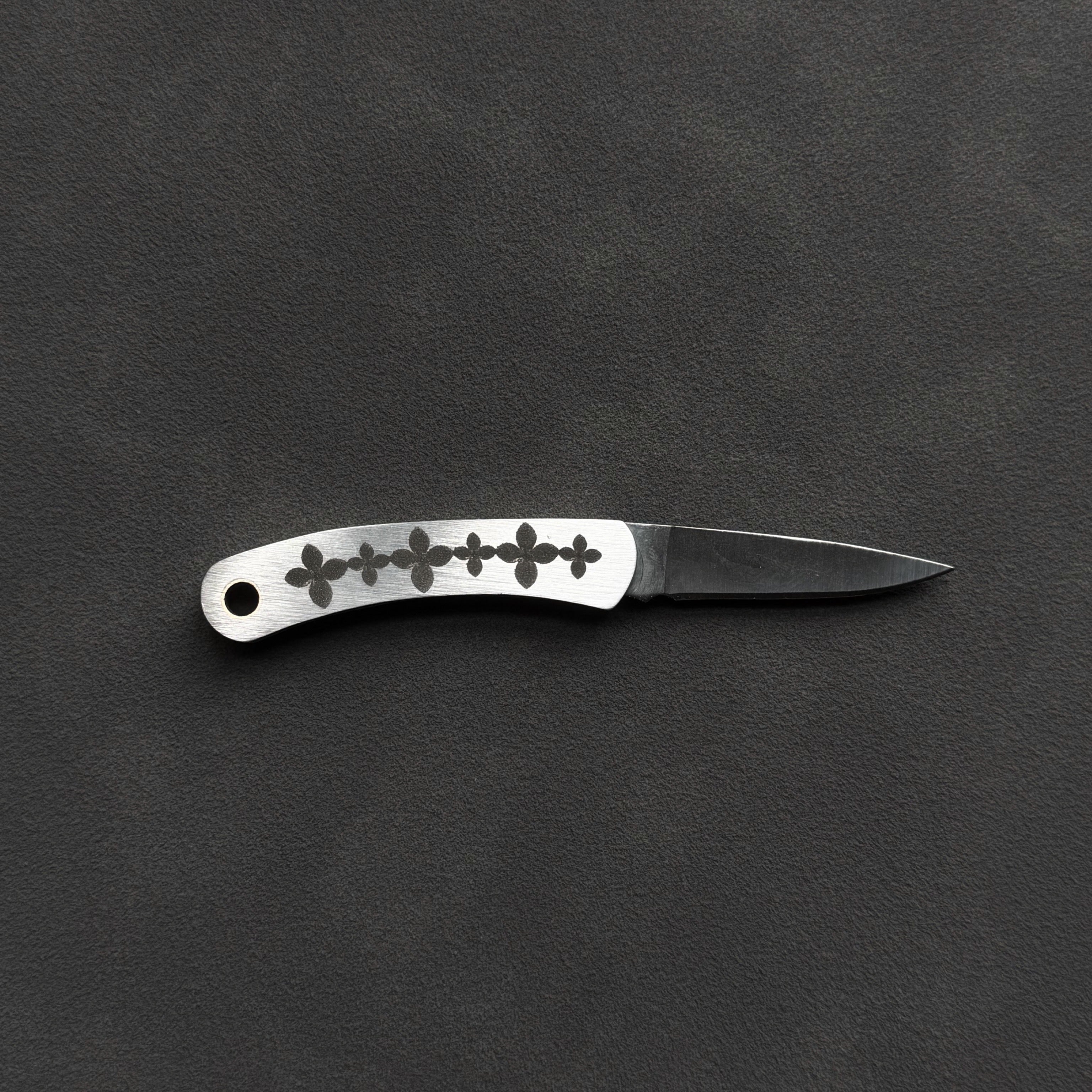 A small folding pocket knife with a silver handle featuring a row of black floral or cross-like cutouts, and a metal blade, displayed horizontally on a dark textured background.