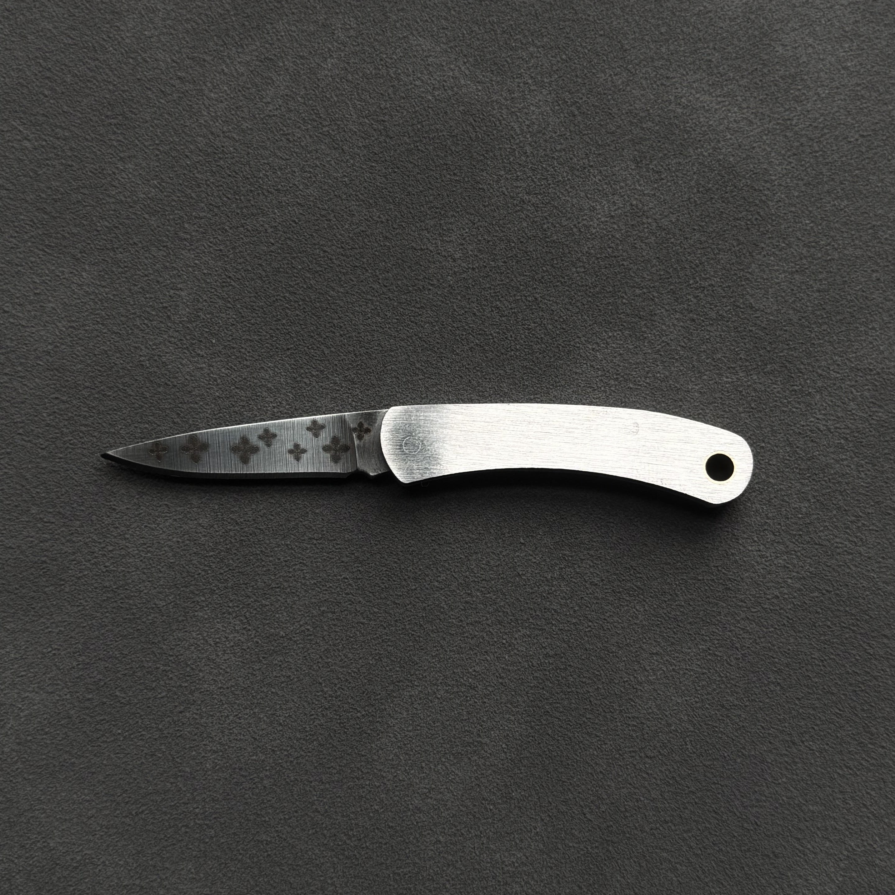 A small folding pocket knife with a satin-finished silver handle and a partially serrated steel blade, displayed horizontally on a dark textured background.